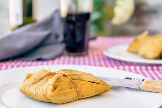 Tamale servito su un piatto bianco su un tavolo tradizionale accanto a un bicchiere di vino rosso. Un tipico panino o pasto latino americano a base di farina di mais e carne. Cibo tradizionale andino. Concetto di cibo tradizionale