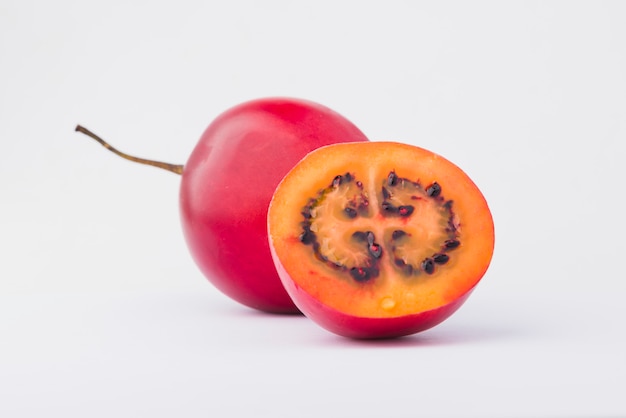 Tamarillo rosso con una fetta su sfondo bianco