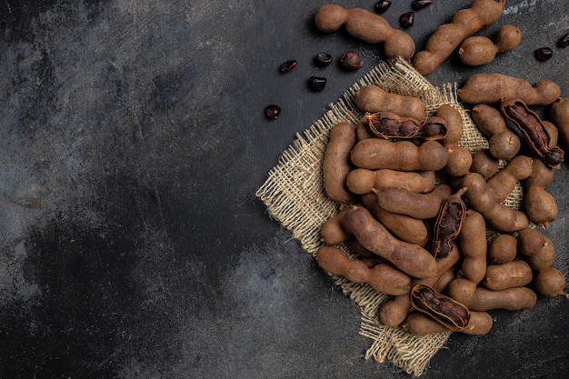 Tamarindi Fagioli Tamarindo in guscio su un blocco di macellaio marrone su uno sfondo scuro menu di banner di frutta sana ricetta posto per testo vista dall'alto