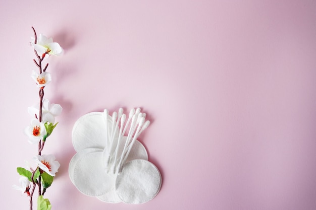 Tamponi di cotone e tamponi con fiori bianchi su sfondo rosa pastello