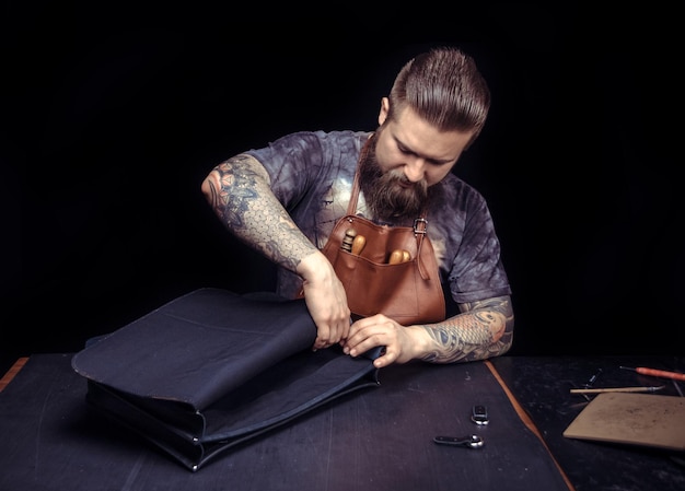Tanner ritaglia articoli in pelle nel suo posto di lavoro./Uomo in pelle che produce nuovi prodotti in pelle nello studio di pelletteria.