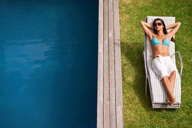 Tanto sole per prendere il sole Una bella giovane donna che si rilassa su una poltrona a bordo piscina