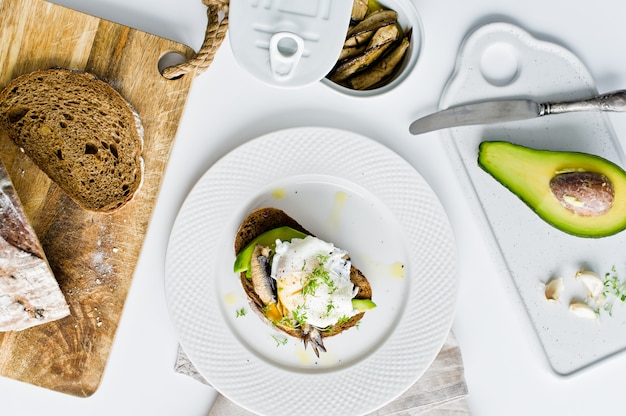 Tapas con avocado, uovo in camicia e spratti.