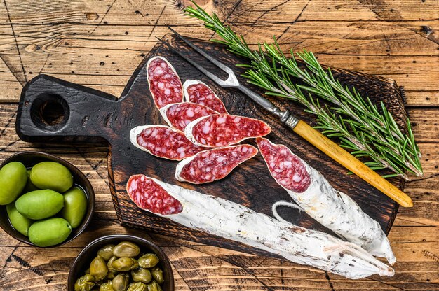 Tapas spagnole Fuet Fette di salame con olive e rosmarino su una tavola di legno.