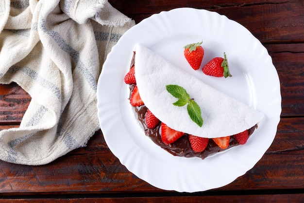 Tapioca fatta in casa o beiju ripieni di fragola e cioccolato su piatto bianco sopra tavolo in legno rustico