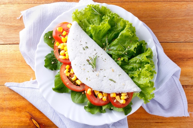Tapioca o beiju con verdure pomodoro rucola mais lattuga in piatto bianco su tavolo in legno rustico Vegan fitness food senza glutine