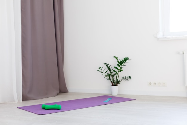 Tappetino da yoga srotolato su pavimento in legno in un moderno centro fitness oa casa con grandi finestre e pareti di mattoni bianchi, spazio confortevole per fare esercizi sportivi, meditazione, attrezzature per lo yoga