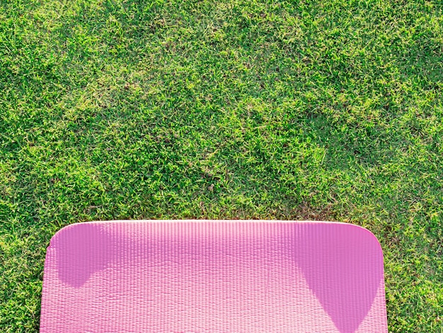 Tappetino yoga rosa adagiato sull'erba verde Nel parco la sera c'era una luce solare morbida I toni della luce calda sono adatti per esercizi di yoga