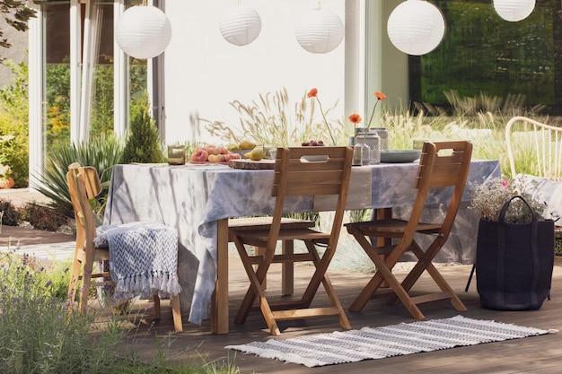 Tappeto accanto a sedie di legno a tavola con cibo sulla terrazza con lampade e fiori