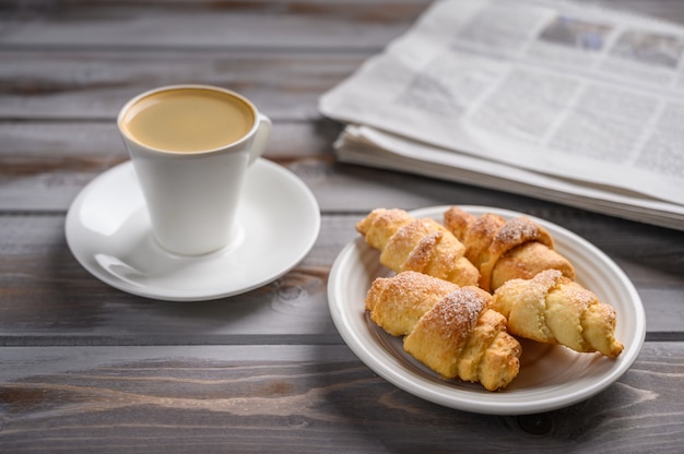 Tappo di caffè e biscotti fatti in casa bagel su una superficie di legno vicino a un fuoco selettivo di giornale