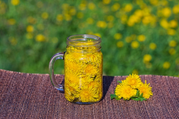 Tarassaco fiore giallo tè bevanda in tazza di vetro sul tavolo nel fondo della natura, all'aperto, si chiuda. Concetto di sana alimentazione