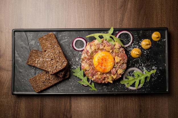 Tartare di manzo con cipolle verdi uovo senape e pane su un piatto nero Vista dall'alto della tartare