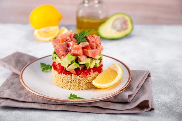 Tartare di salmone con pomodori, avocado e quinoa su un piatto e tavolo grigio chiaro.