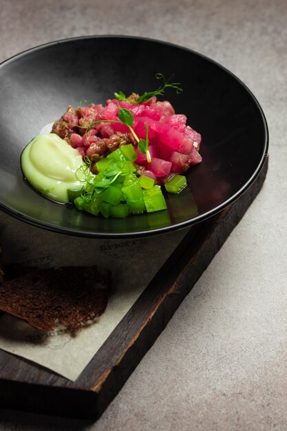 Tartare di tonno con cetriolo sottaceto e salsa su piatto nero