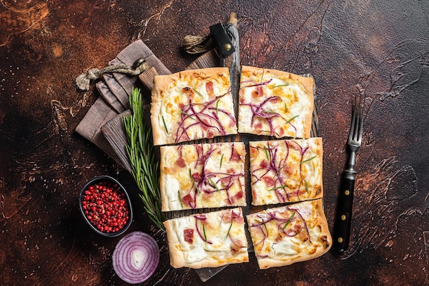 Tarte flambee francese con crema di formaggio, pancetta e cipolle. Flammkuchen dalla regione dell'Alsazia. Sfondo scuro. Vista dall'alto.