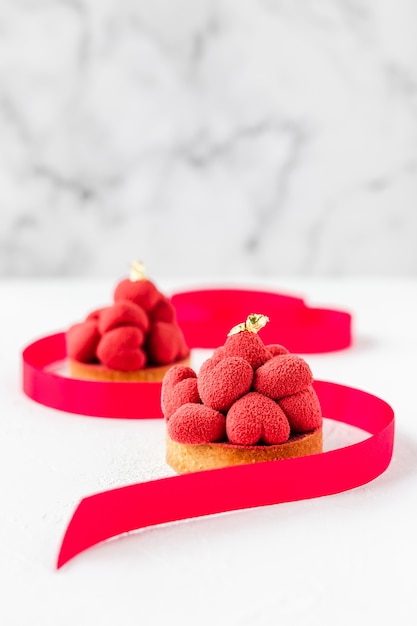 Tartelette dolci al dessert con cuori di mousse rossa in cima, decorate con un nastro