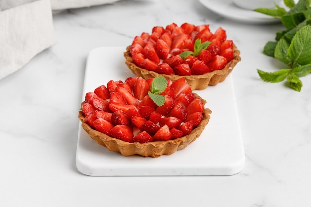 Tartellette di crema di fragole su fondo di marmo bianco Mini cheesecake con fragole