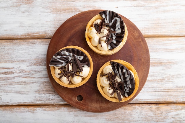 Tartellette dolci con crema di cioccolato e formaggio su fondo piatto in legno bianco