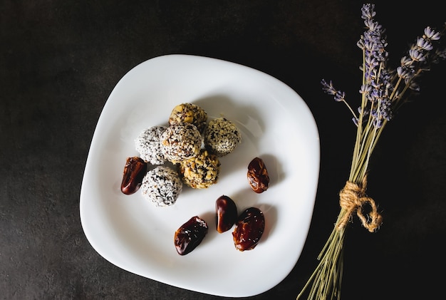 Tartufi crudi fatti in casa con cacao, noci, cocco e datteri su piatto bianco e tavolo grigio. Lavanda su sfondo. Caramelle vegane, biologiche e salutari.