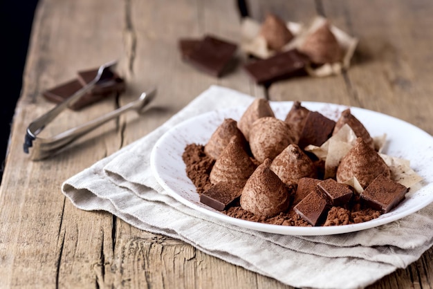 Tartufi di cioccolato fatti in casa con polvere di cacao su un piatto bianco Vecchio fondo di legno Caramelle saporite