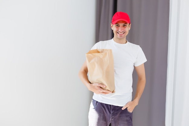 Tasca di carta e contenitori per alimenti nelle mani di un fattorino sorridente. Servizio di qualità di un ristorante.