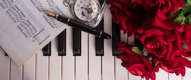 Tasti di pianoforte, spartito musicale, penna stilografica, orologio antico e bouquet di rose