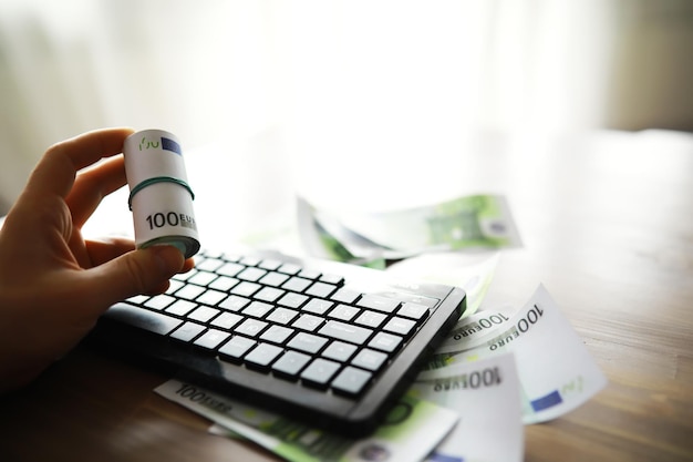 Tastiera del computer e una manciata di banconote da 100 euro sul tavolo Il lavoro di un programmatore e blogger su Internet