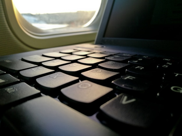 Tastiera del computer portatile vicino al sedile della finestra della cabina dell&#39;aeroplano che lavora in movimento