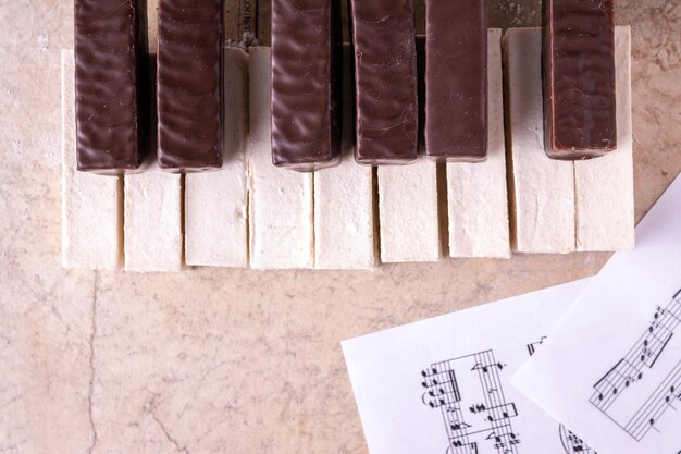 Tastiera di pianoforte fatta di marshmallow bianchi e cioccolato sullo sfondo di carta da musica