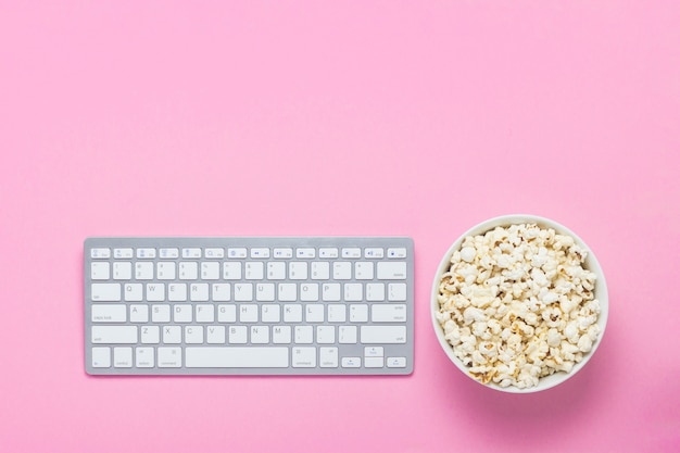 Tastiera e ciotola di popcorn su un rosa. concetto di guardare film, programmi TV e spettacoli online. Vista piana, vista dall'alto.