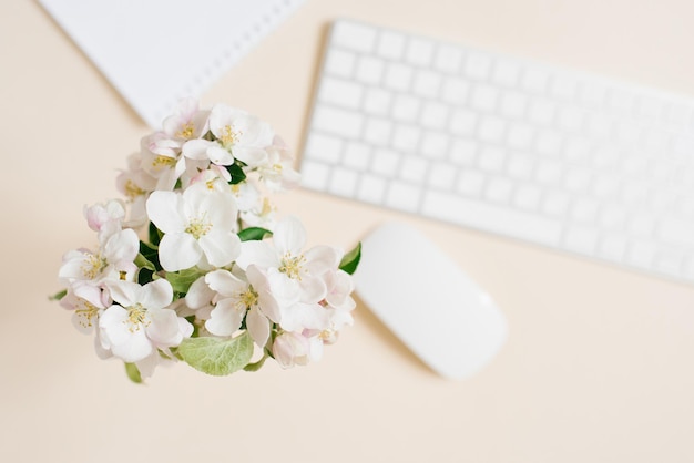 Tastiera foglio bianco di carta e mouse e fiori di mela bianca in un vaso