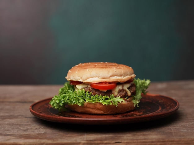 Tasty Burger giace su un piatto di argilla contro un tavolo di legno Una foglia di insalata verde succosa e un pomodoro rosso