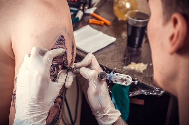 Tattoo artist al lavoro in tattoo parlour./Tattooer in posa in tattoo studio.