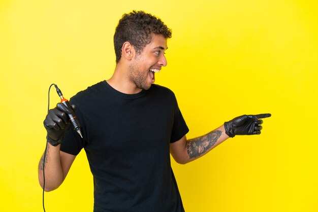 Tatuatore uomo brasiliano isolato su sfondo giallo che punta il dito sul lato e presenta un prodotto