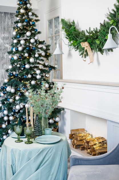 Tavola apparecchiata per la cena di Natale o Capodanno con decorazioni di candele tovaglia e tovaglioli sullo sfondo di un albero di Natale in un appartamento