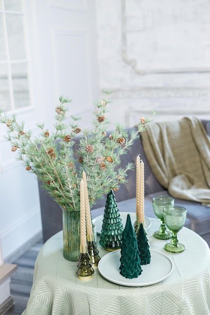 Tavola apparecchiata per la cena di Natale o Capodanno con decorazioni di candele tovaglia e tovaglioli sullo sfondo di un albero di Natale in un appartamento