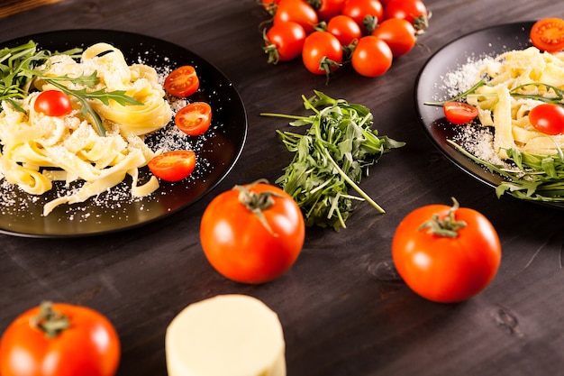 Tavola con pasta sana e gustosa accanto a pomodorini, parmigiano e verde