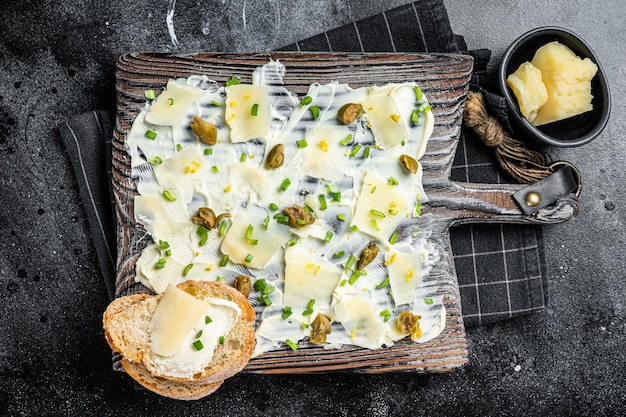 Tavola di burro con erbe aromatiche scorza di limone capperi parmigiano e sale marino Butterboard Sfondo nero Vista dall'alto