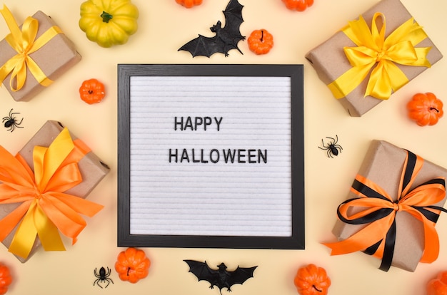 Tavola di feltro con la scritta Happy Halloween sullo sfondo di regali, zucche e ragni su fondo beige. Vista dall'alto.