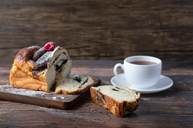 Tavola di legno di torta con semi di papavero e una tazza di tè posta su un tavolo.