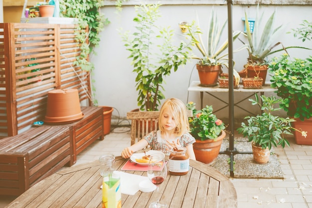 Tavola di seduta all&#39;aperto del bambino femminile che mangia prima colazione