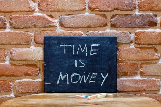 Tavola nera con la frase "Il tempo è denaro" annegata a mano su un tavolo di legno sullo sfondo di una parete di mattoni per una presentazione aziendale