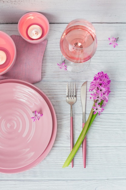 Tavola rustica rosa con fiori di giacinto viola candele tovagliolo di lino e bicchiere di vino rosato su tavolo di legno bianco