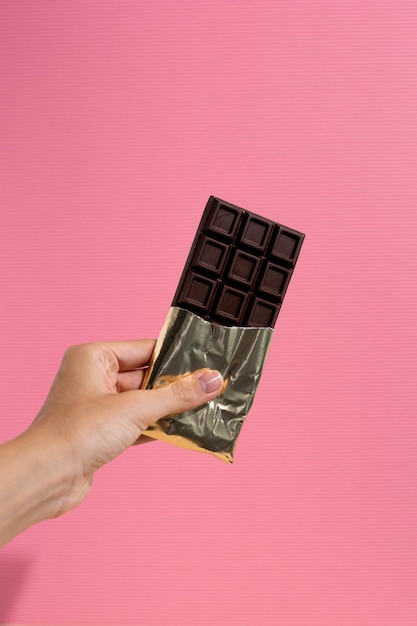 Tavoletta di cioccolato fondente in mano su sfondo rosa