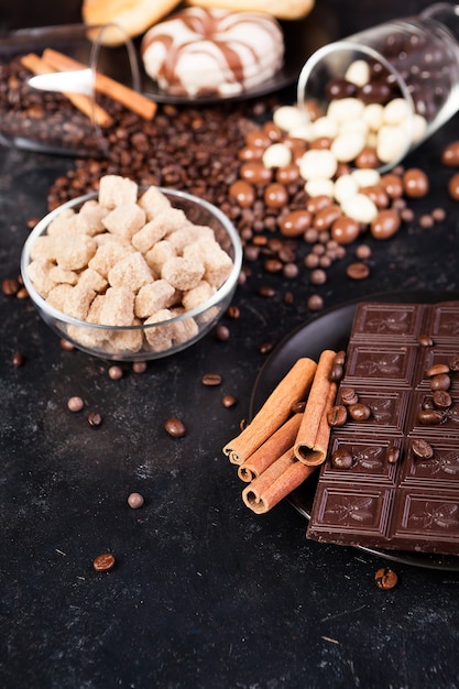 Tavolette di cioccolato accanto a panini alla cannella e altri dolci e caramelle su uno sfondo di legno