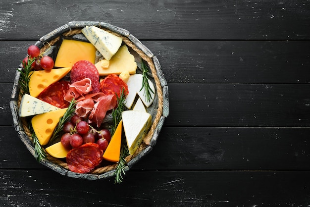 Tavolo antipasti con antipasti italiani e vino in bicchieri Formaggio vino salame e prosciutto su uno sfondo di pietra nera Vista dall'alto Spazio libero per il testo