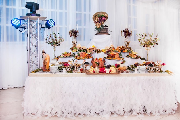 Tavolo buffet con snack di carne maialini al forno in pasta formaggio tacchino con frutta decorata con candelabri e grammofono