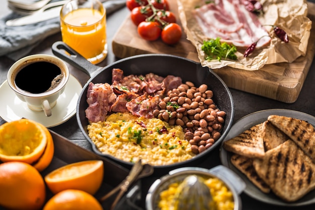 Tavolo completo della colazione inglese. Uova strapazzate bacon grigliato fagioli pane tostato succo d'arancia e caffè.