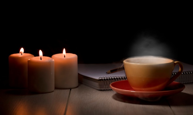 Tavolo con candele accese taccuino matite libri tazza gialla con fumo di vapore