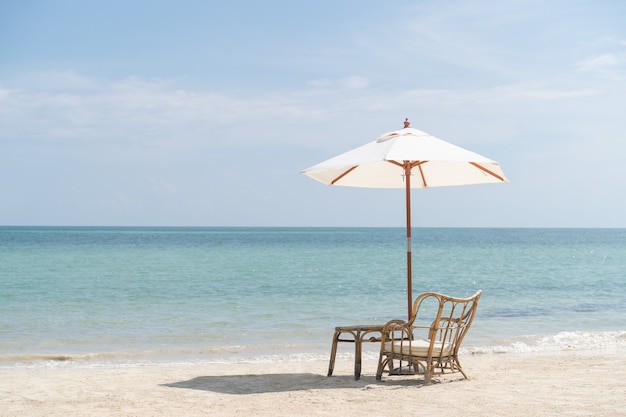 Tavolo con sedie e ombrellone allestito per una romantica cena in spiaggia, cielo e mare sullo sfondo.